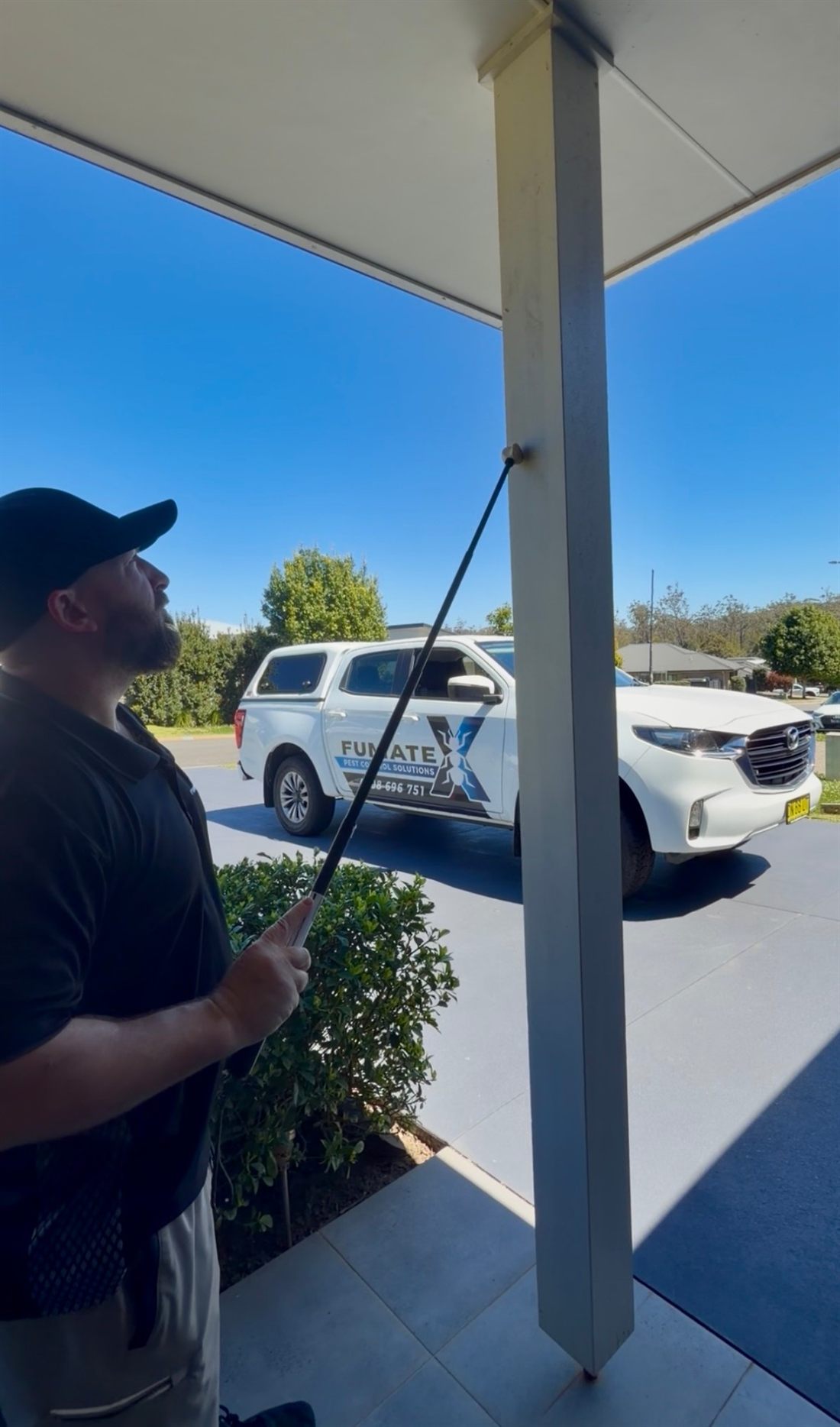 Fumatex technician treating under the eaves with a telescopic pole, work ute in the background